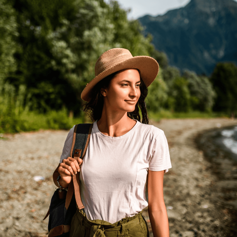 Photo of a girl travelling wearing a straw hat with mountains in the background.